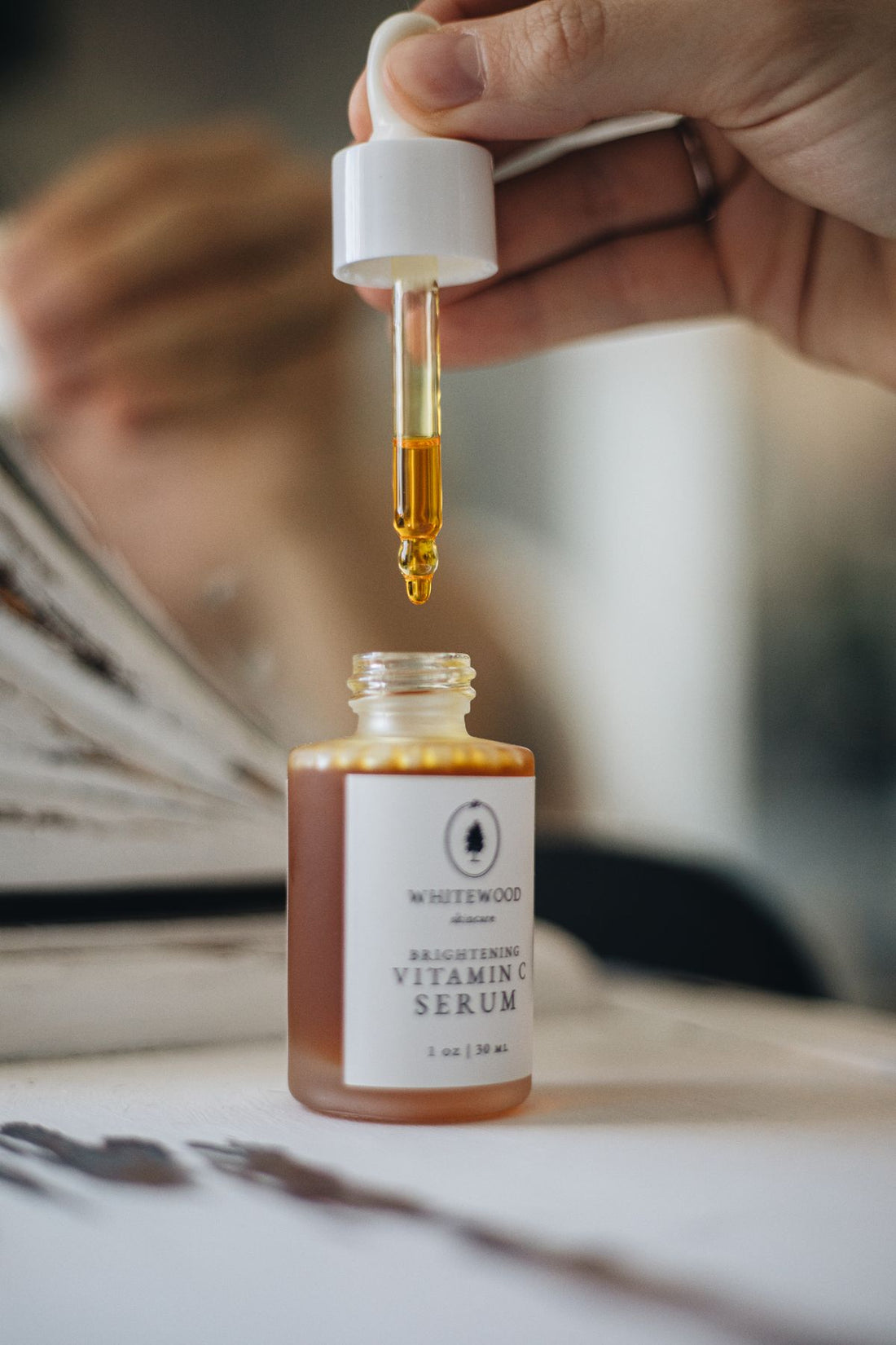 Amber glass serum dropper bottle on a pale linen surface beside dried botanicals in soft natural light