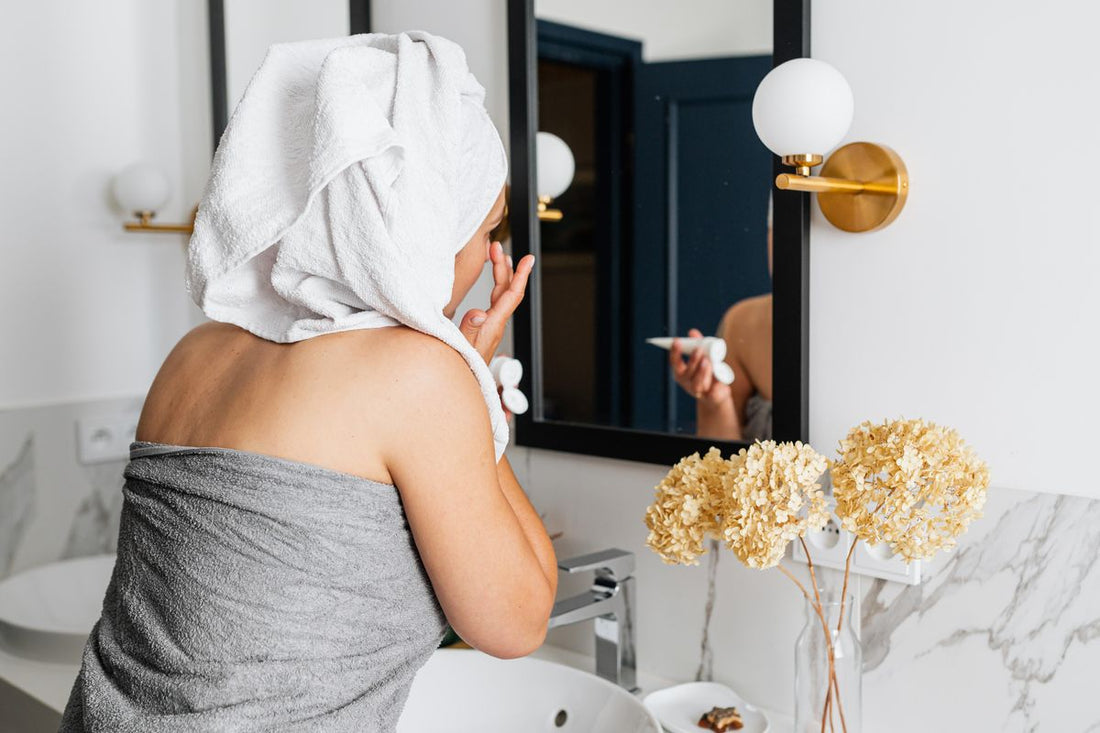Woman applying face cream in front of a bathroom mirror as part of a morning skincare routine