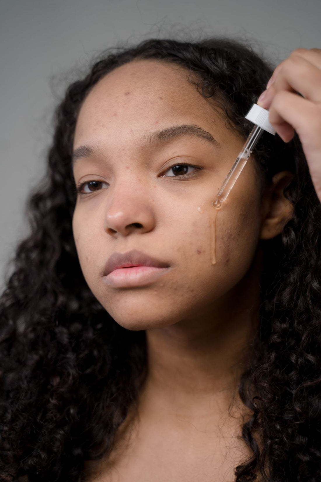 Portrait of a woman applying hydrating serum to her cheek, illustrating a winter skin barrier care routine